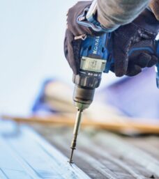 A person using a drill to fasten a piece of metal roofing